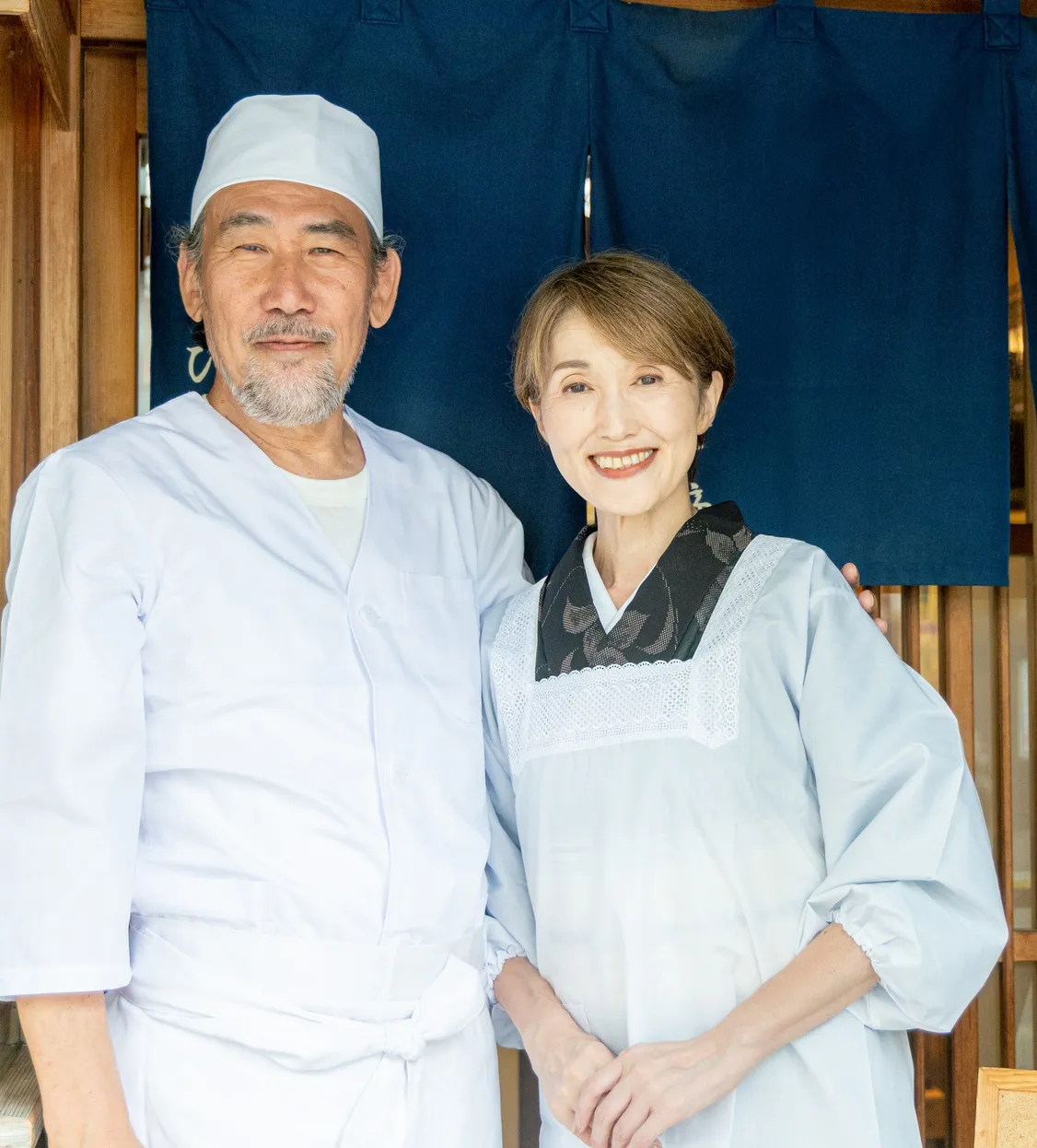 のれんの前に立つ店主夫婦のような男女